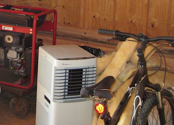A black bicycle parked next to a pile of yellow fiberglass scraps. There is a white dehumidifier and a red generator next to it.