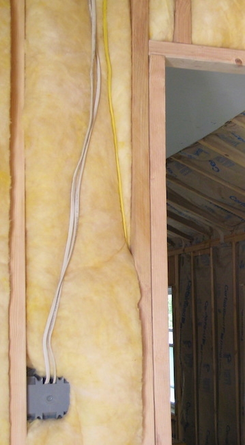 Yellow fiberglass lining a doorway inside of a room with more fiberglass batts lining the ceiling and walls in the room behind it.