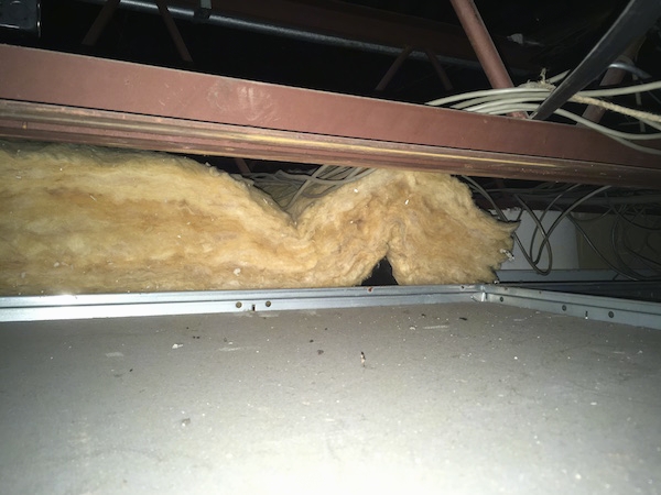 A fiberglass batt laying on top of a ceiling panel with wires and red beams all around it