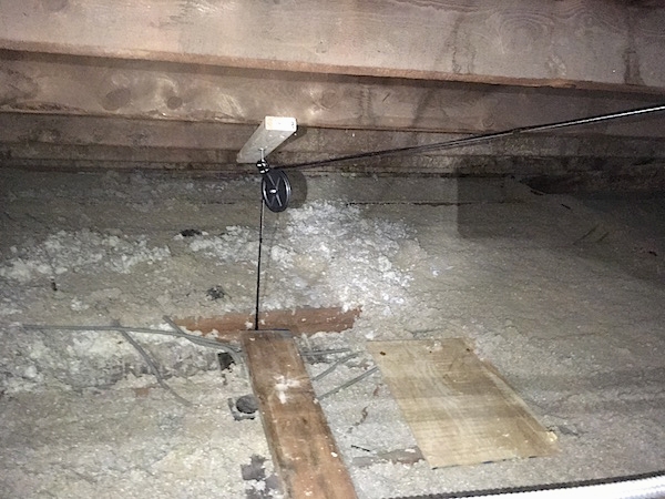 An attic with gray blown in insluation with pully wires that old up the chandeliers below.