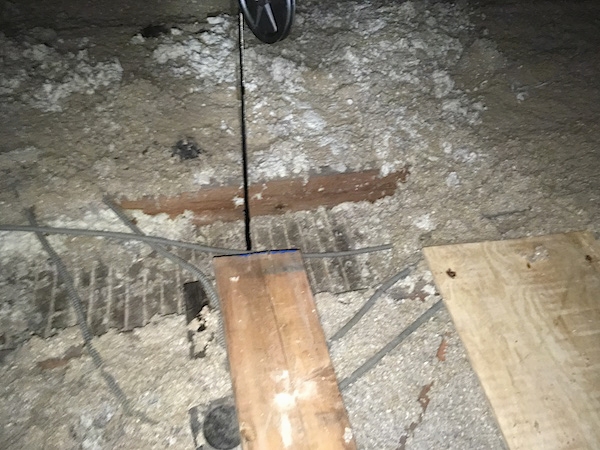 An attic with gray blown in insulation with wood boards and wires going into the floor to the ceiling below.