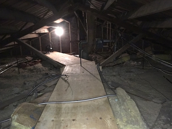 A cat walk in an attic that has yellow fiberglass batts and gray blown in insulation.