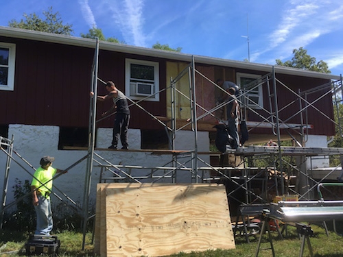 Scaffolding set up in front of the red barn with men taking the fiberglass batts out of the walls. The lower part of the barn is a white stone wall.