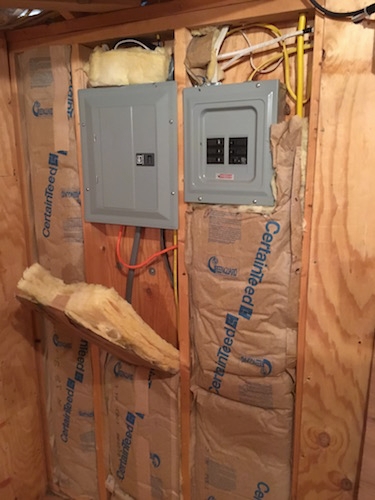 An interior wall of a barn showing the electrical boxes with yellow fiberglass batts around them.