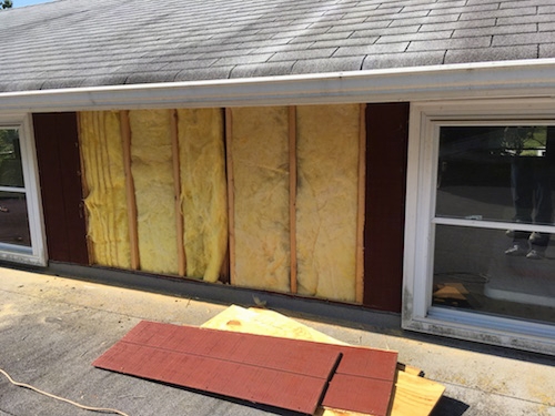 A wall of a red barn with T1-11 taken off showing the yellow batts of fiberglass underneath.