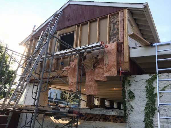 Side angle view - pink fiberglass batts falling out of a wall of a barn from the second story room with ladders and scaffolding set up.