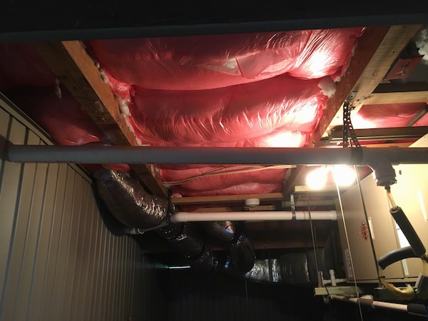 fiberglass insulation tacked to the ceiling on the lower level of a beach house with flex ducts and electric panels and pipes near it