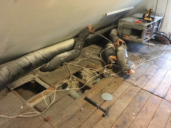 An attic floor with the HVAC system being removed, boards removed and flex ducts and wires all over.