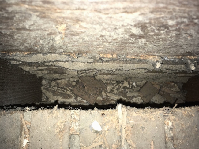 Looking into the cavity of an attic floor that was under a  HVAC system. The area is tan and dirty.