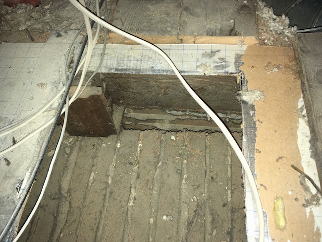 A hole in a  dirty attic floor showing old white flooring where the HVAC unit was resting.