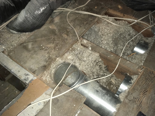 Some boards removed from an attic floor exposing gray blown-in loose insulation along with duct work, both flex and hard and white wires.