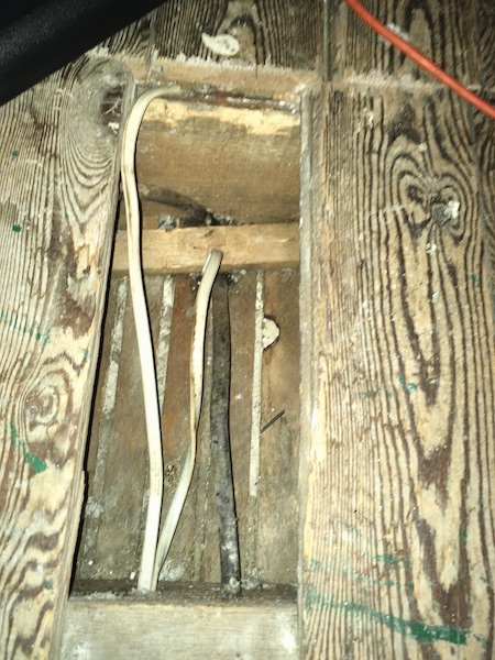 Looking down into a hole in a wooden floor with white wires running through it.