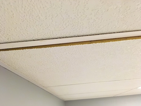 A white ceiling panel with a crack between the panels showing how it is made of yellow fiberglass.