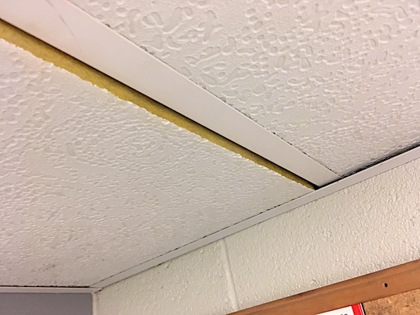 The seam of a white ceiling panel showing the edge made of yellow fiberglass.