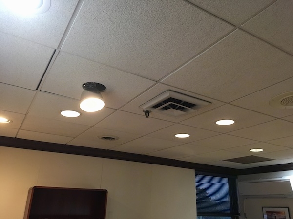 The ceiling of an office with square white tiles with lighting and duct work vents in it.