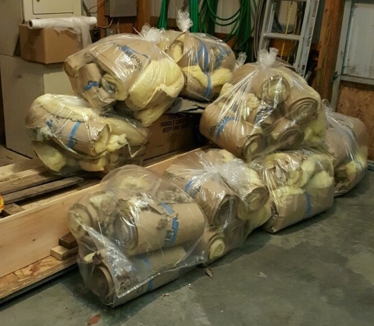 Clear trash bags on a floor full of rolls of yellow fiberglass bats piled up awaiting to be tossed into the dumpster.