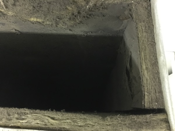 Looking down the inside of a fiberglass lined duct. It has a thick layer of dirt on top of the paper liner. The glass is falling apart and so is the outer paper.