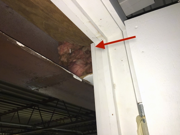 A bunch of fiberglass shoved into the hole of a beam in an industrial building with a red arrow pointing to the insulation