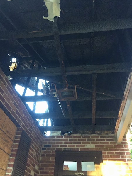 Looking up into the ceiling of a house that burned down. The walls are brick and the beams are chared.