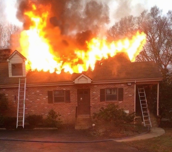 A house activly burning down with flames coming out of the roof.