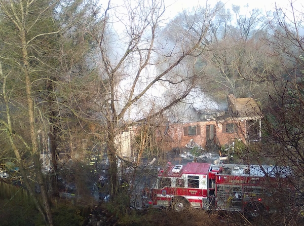 View from above of a house with smoke coming out of the roof and a red fire truck parked in the driveway.