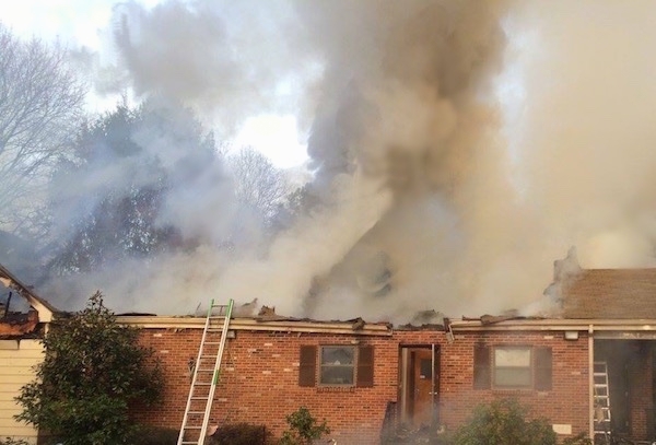 A burning house with the roof gone and smoke coming out of it.