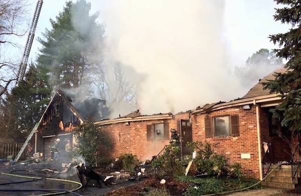 A brick house with the roof gone and smoke coming from it.