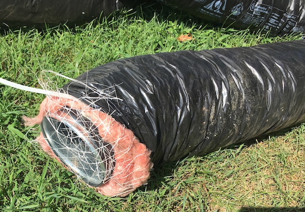 A black flex duct with pink fiberglass hanging out the end laying in the grass out in a yard after being removed.