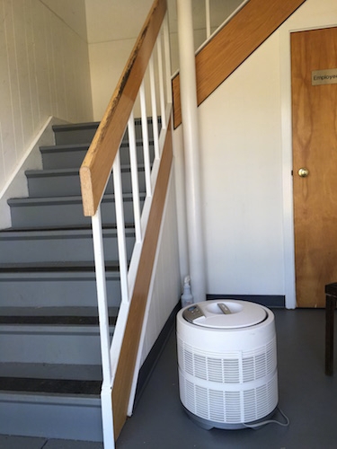 A round white HEPA filter sitting on a gray floor with a staircase next to it.