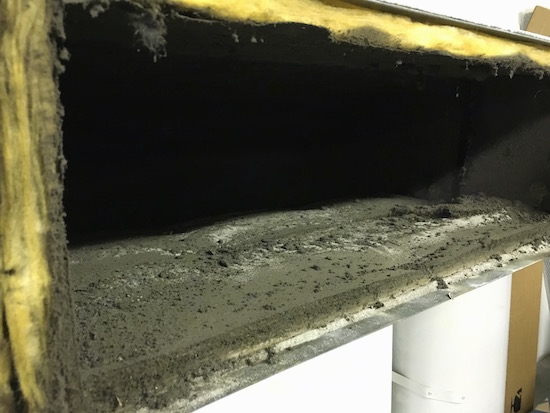 A section of a fiberglass lined duct with lots of black dirt all over the inside