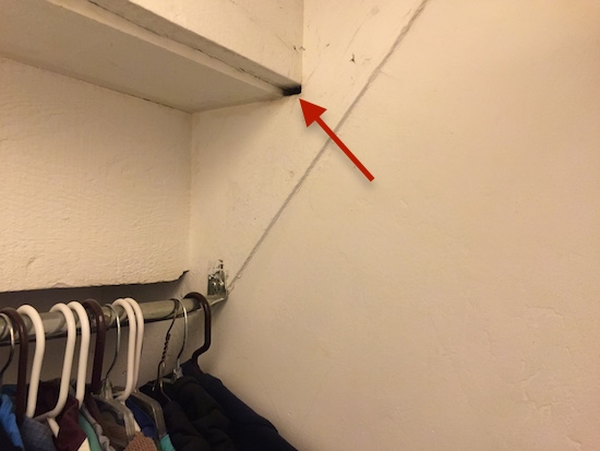 a bedroom closet with clothes hanging up and a red arrow pointing to a hole in the wall