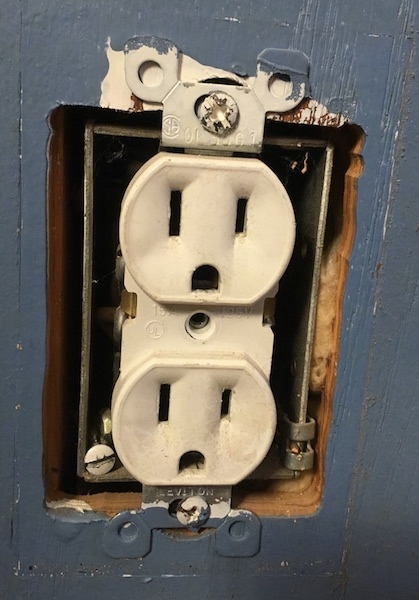 Close up of an electrical outlet that has the cover removed showing yellow fiberglass in the wall.