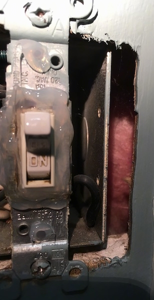 Close up of a light switch that has the cover removed with pink fiberglass insulation showing in the wall.