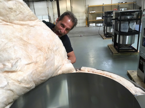 A man in a shop pretending to take a bite out of an insulation batt that he is installing. The man is not wearing a mask or gloves.