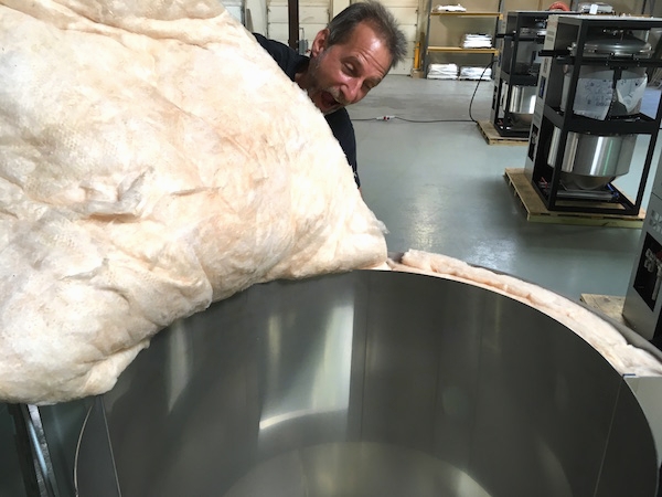 A man pretending to bite a batt of fiberglass insulation as of it is cotton candy in a machine shop.