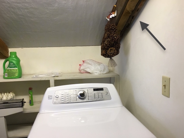 A laundry room in a home showing fiberglass shoved in a crack in the wall above a dryer