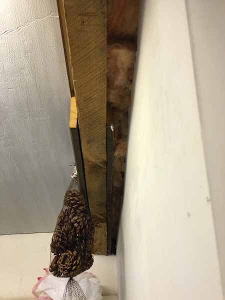 Closer view - A laundry room in a home showing fiberglass shoved in a crack in the wall with a bag of scented pinecones hanging on the beam as an air freshener