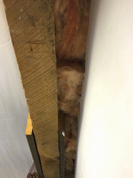 close up view of fiberglass shoved in a crack in a wall of a laundry room