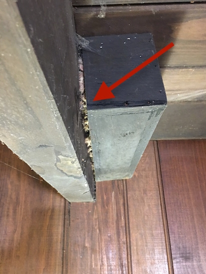 a red arrow pointing to a crack between a wooden beam and wooden box in a ceiling with fiberglass exposed in the crack