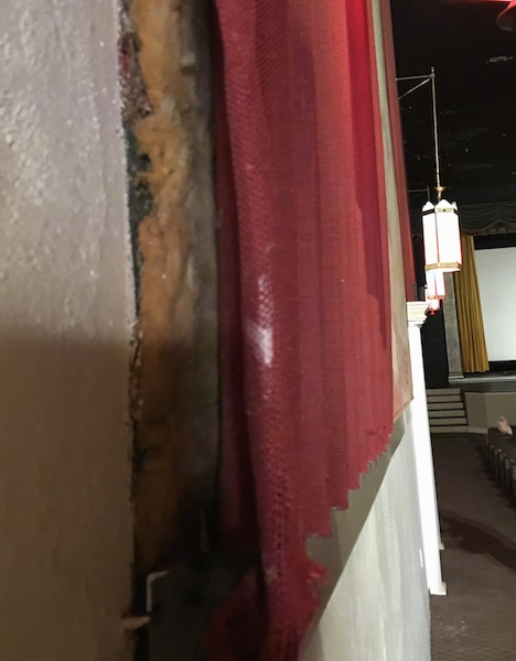 A wall in a movie theater with a piece of fabric hanging as a decoration to hide the exposed fiberglass