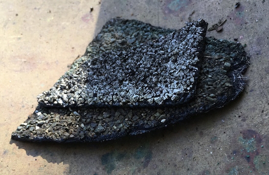 A corner of a roo shingle placed on top of a copper surface.