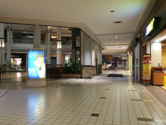 A big empty shopping mall with closed stores and a staircase in the background. It looks like a ghost town.