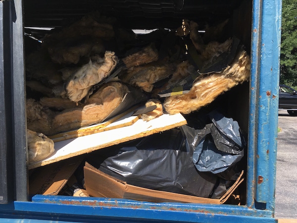 A blue dumpster full of fiberglass insulation that was removed from a vestibule.