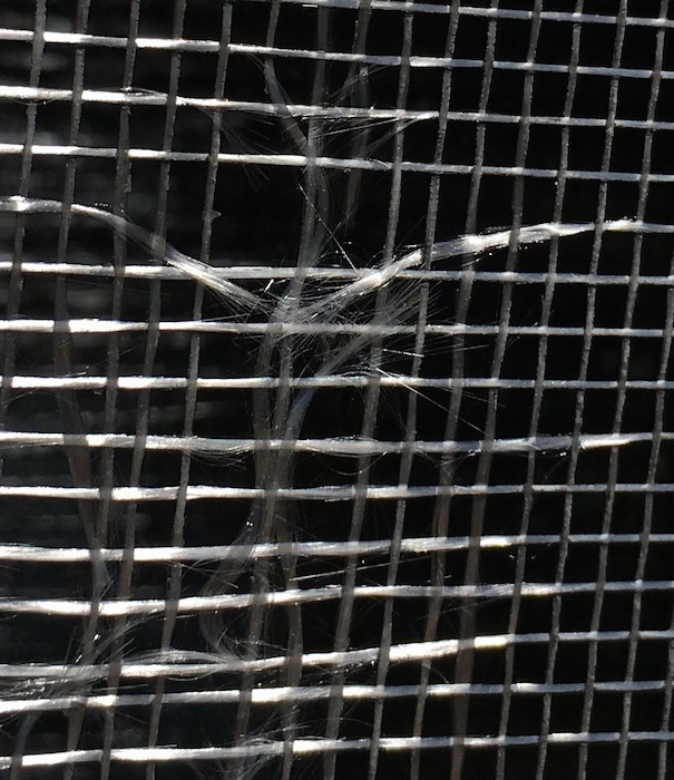 Close up of a window screen with glass fiber strands fraying.