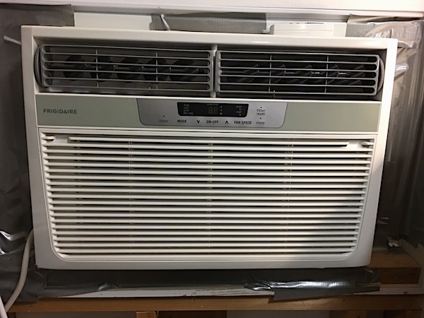 A white Frigidaire window heat pump unit inside of a window with duct tape around the edges of the window sill.