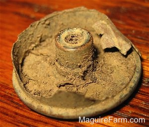 The Underside of the 12 gauge shotgun shell. It has a lot of dirt caked in it
