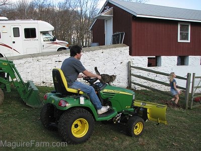 A man riding a John Deere X728 Ultimate™ Tractor through an open gate with a girl standing there waiting to reclose the gate.