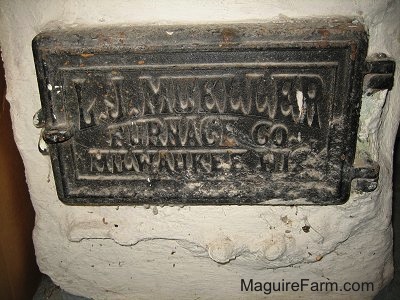 A black door in a cement wall that says 'Old Furnace Cover - L. J. Mueller Furnace Co. Milwaukee WI'