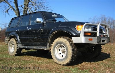 The front of a jacked up black 1996 Toyota Land Cruiser with mud on the large tires with a front bumper guard.