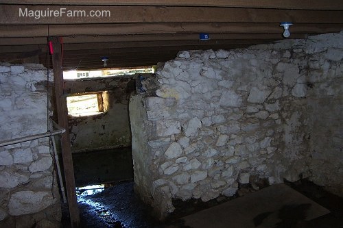 The inside of an old stone spring house showing the lights on the ceiling. It has two rooms with water inside one of the rooms.